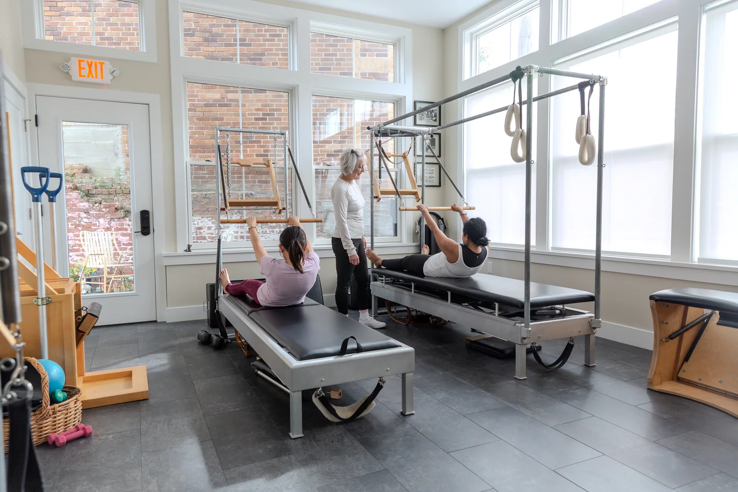 Sheila guiding two clients on the studio’s classical Pilates apparatus